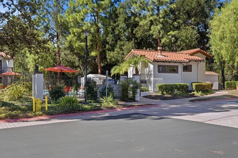 A house with a red roof is surrounded by trees and a fence.