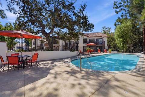 A pool with a table and chairs in front of a house.