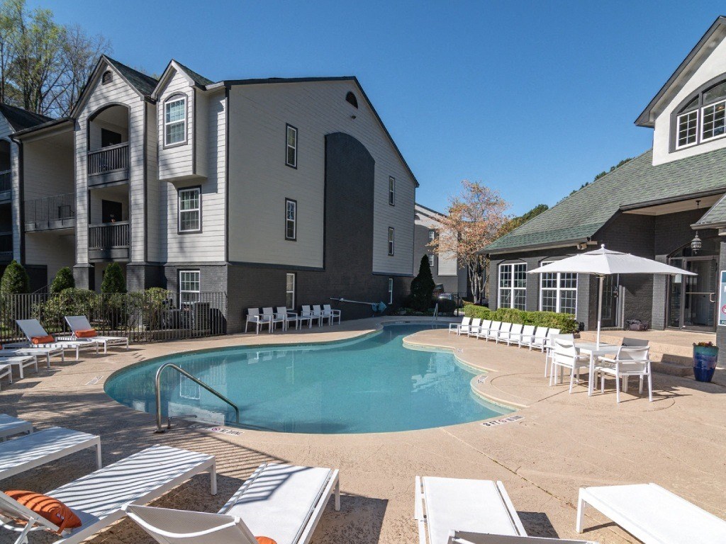 a large swimming pool with chairs and umbrellas in front of a building