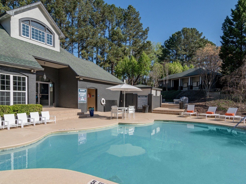 a swimming pool with chairs and umbrellas in front of a house