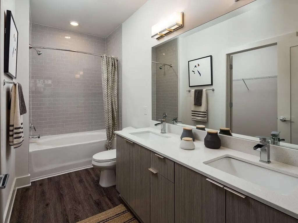 A bathroom with a white toilet, a bathtub with a shower curtain, a sink, a mirror, and a rug on the floor.