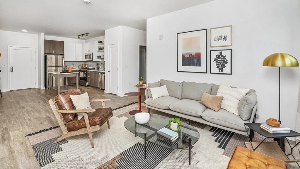 A modern living room with a grey sofa, a glass coffee table, and a wooden chair.