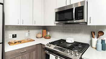 A modern kitchen with a stove, microwave, and wooden cutting board.