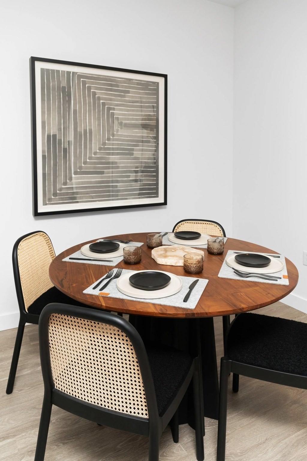 A table with plates and cutlery is set for two with a framed artwork on the wall behind it.