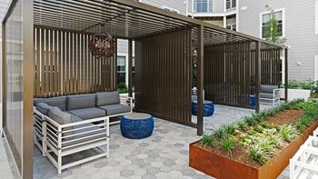 A patio with a grey sofa and a wooden pergola.