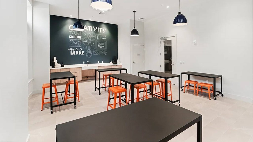 A black table is in the middle of a white room with a chalkboard on the wall.