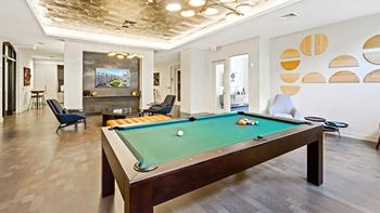 A pool table is in the middle of a room with a chair and a painting on the wall.