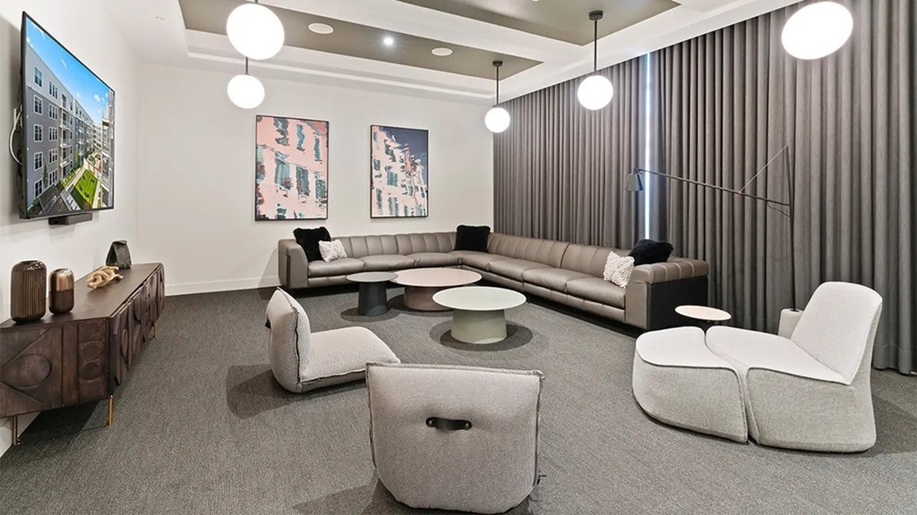 A modern living room with a grey sofa, two grey armchairs, a coffee table, and a wooden sideboard.