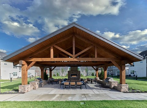 A wooden pavilion with a stone base is surrounded by a paved area and grass.