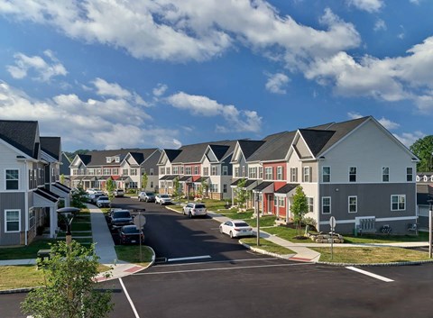 A street view of a residential area with houses on both sides and cars parked along the curb.