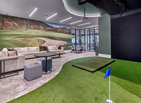 A room with a golf putting green and a large picture of a golf course on the wall.