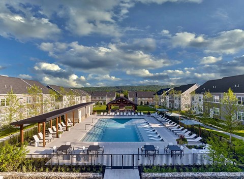 A large outdoor swimming pool surrounded by lounge chairs and a wooden pavilion.
