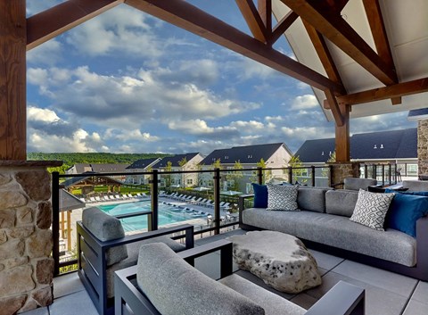 A patio with a couch and a table with a view of a pool and houses.