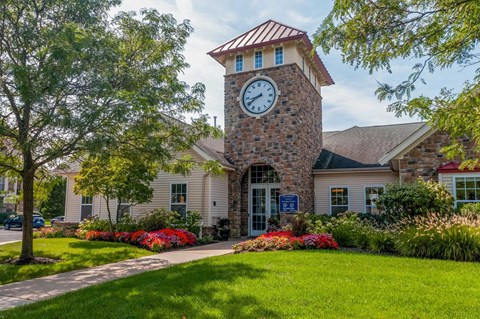 A clock tower stands in front of a building with a green lawn and trees.