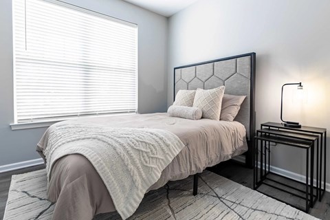 A bedroom with a bed, a nightstand, and a window with blinds.