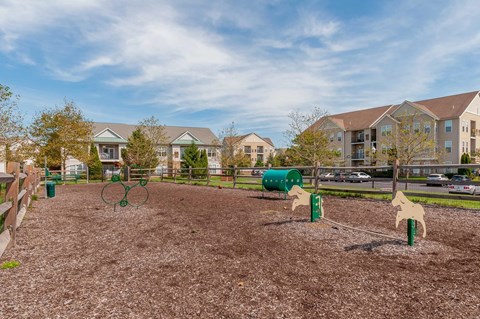 A playground with a swing set and a green barrel.