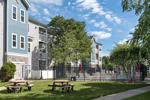 A sunny day at a park with picnic tables and apartment buildings in the background.