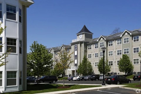 A large apartment complex with a clock tower in the middle of a parking lot.