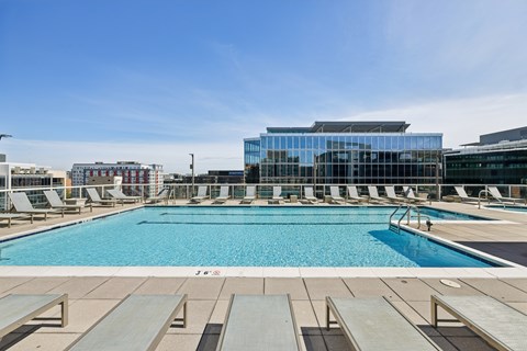 A large swimming pool with sun loungers and a building in the background.