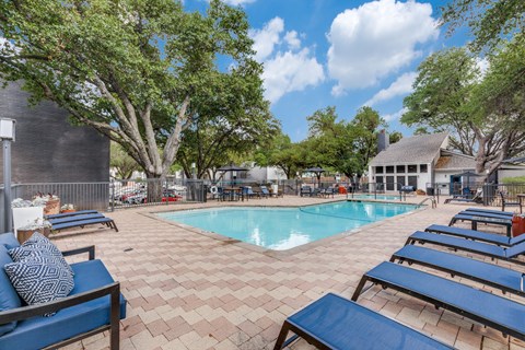 Austin, TX, Apartments with In-Unit Washer and Dryer - Argosy at Crestview - Outdoor Swimming Pool With Blue Lounge Chairs, Patio Seating, Mature Trees, And A Bright Sky.