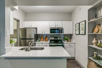 A modern kitchen with a stainless steel refrigerator, a white countertop, and a green plant on the counter at Canyon Ridge, Austin, Texas