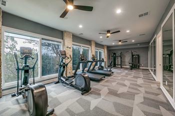 A spacious gym with treadmills, elliptical machines, and a fan at Canyon Ridge, Austin, TX, 78753