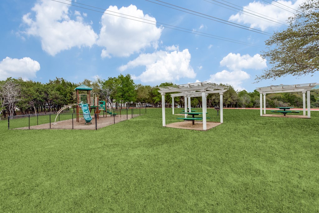 A playground with a green slide and white pergola at Canyon Ridge, Austin, 78753