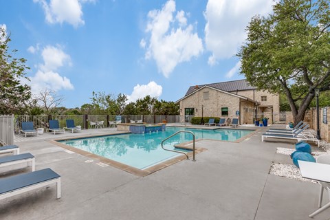Austin, TX, Apartments With In-Unit Washer and Dryer - Canyon Ridge - Resort-Style Swimming Pool With Lounge Seating, Poolside Water Feature, Stone Clubhouse, and Mature Trees.