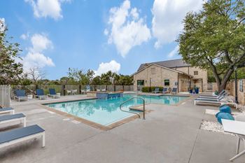 A large outdoor swimming pool with lounge chairs and a building in the background.