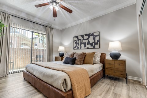 A bedroom with a bed, a ceiling fan, and a painting on the wall.