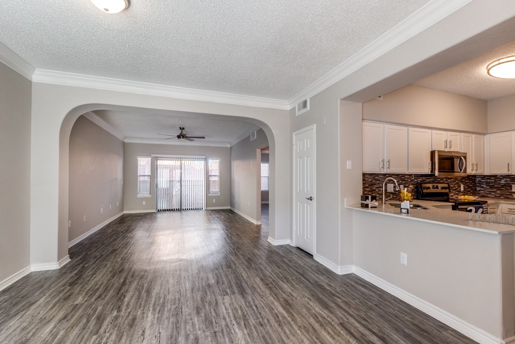 an empty living room with a kitchen and a ceiling fan