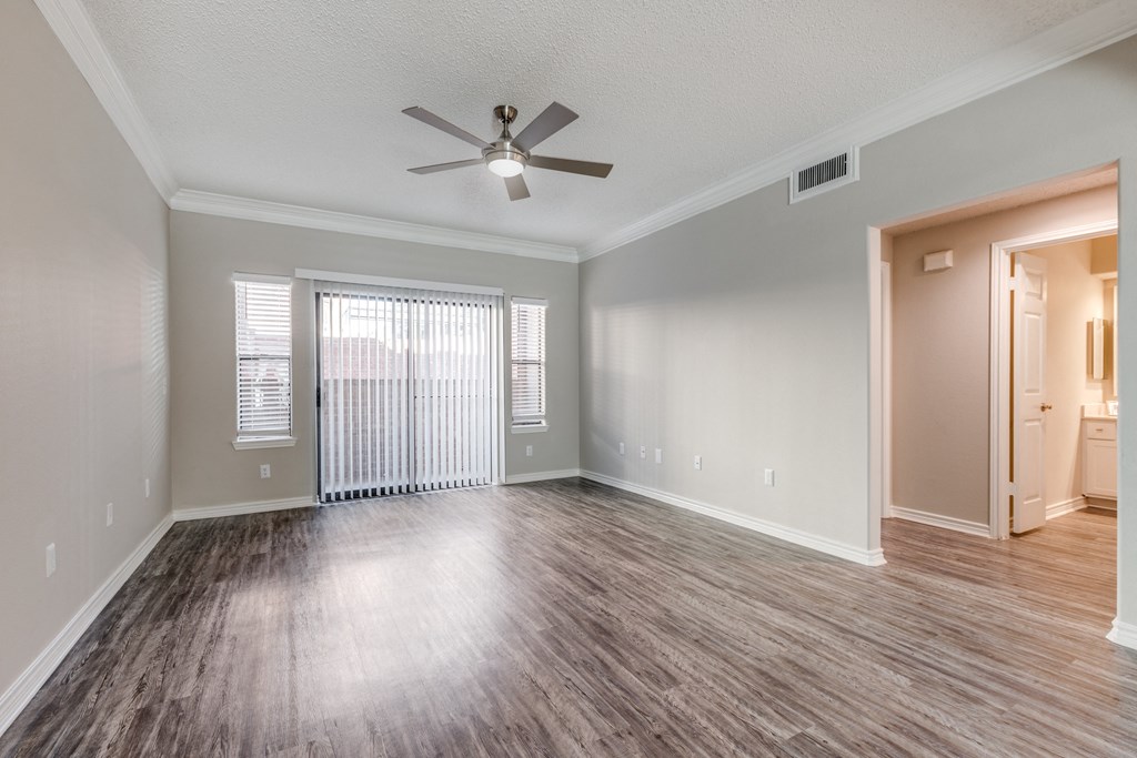 Apartments In Houston, TX - San Montego - Living Room With Faux Wood Flooring, High Ceilings, Ceiling Fan, Large Windows, And Access To Patio Or Balcony Area