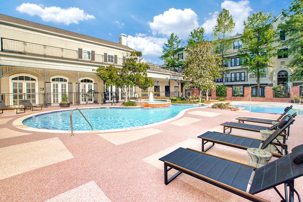A pool surrounded by lounge chairs and trees.