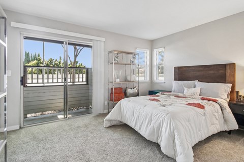 A bedroom with a large bed and a sliding glass door leading to a balcony.