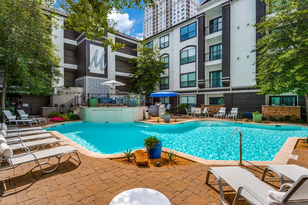 a swimming pool with chairs and umbrellas in front of an apartment building
