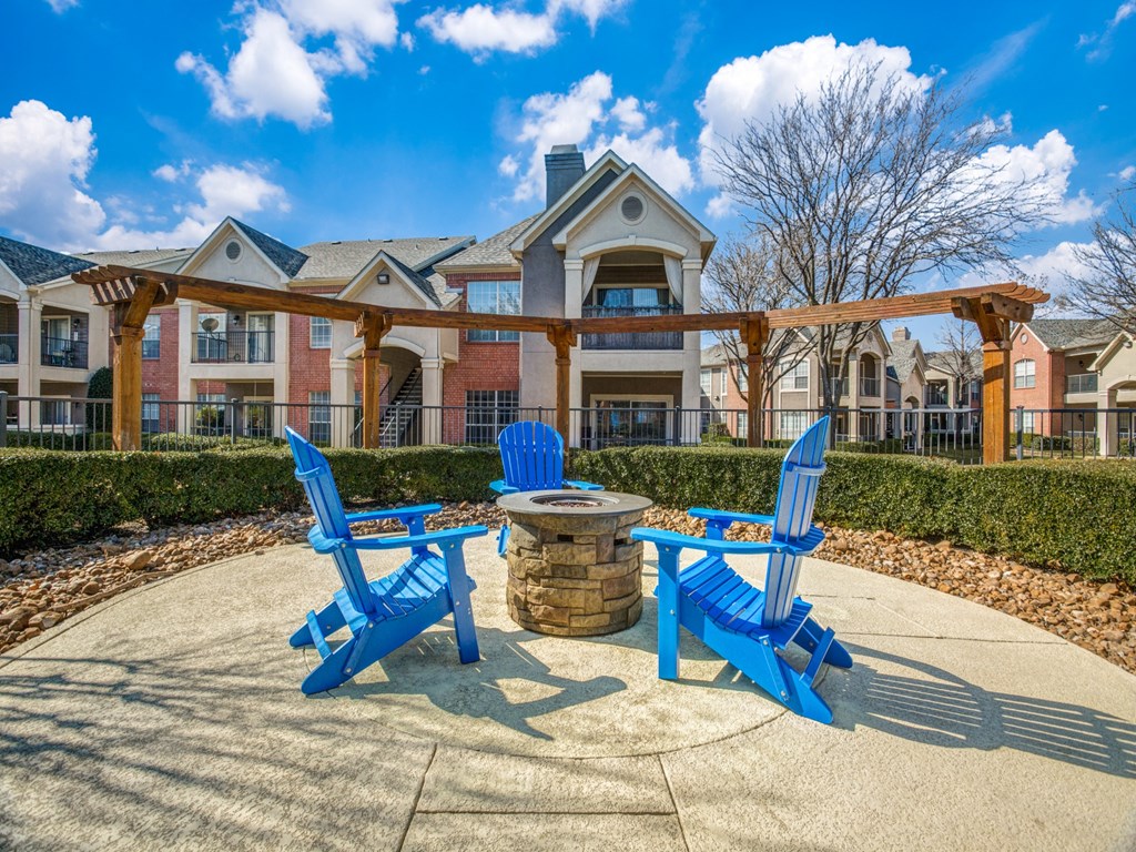 a patio with blue chairs and a fire pit in front of an apartment building
