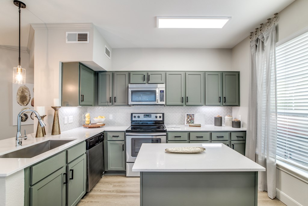 A kitchen with green cabinets and a white island.