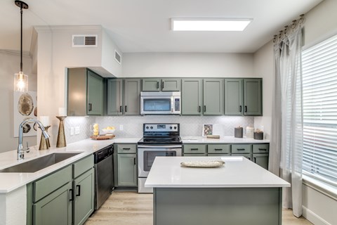 A kitchen with green cabinets and a white island.