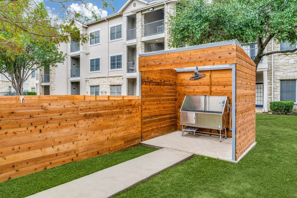 Apartments for Rent in Wells Branch Austin TX - Parkside Crossing - Wooden Dog Wash Station with Concrete Path, Manicured Lawn, and View of Apartment Buildings