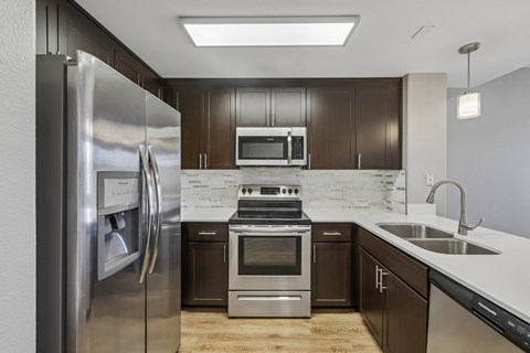 A modern kitchen with dark brown cabinets and stainless steel appliances.