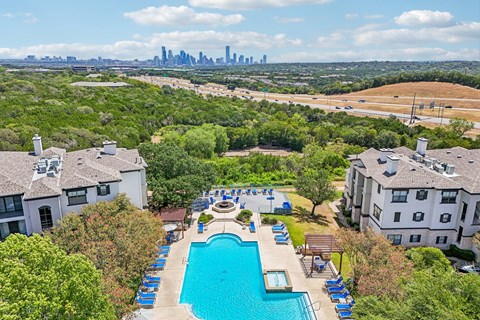 A swimming pool surrounded by trees and buildings with a city skyline in the background.