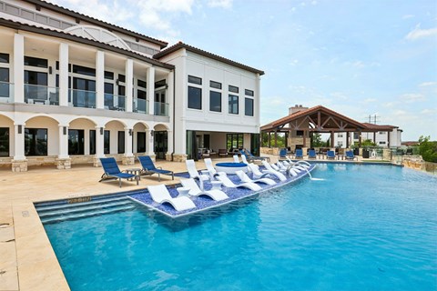 A large swimming pool with lounge chairs in front of a white building.