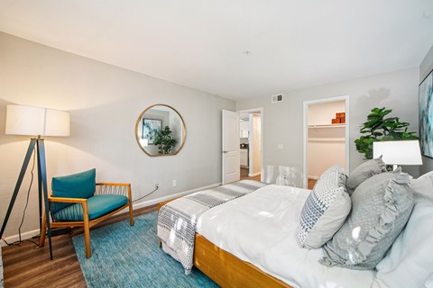 A bedroom with a bed, chair, and a mirror on the wall.