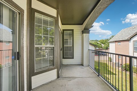 A balcony with a black railing and a view of a blue sky with clouds.