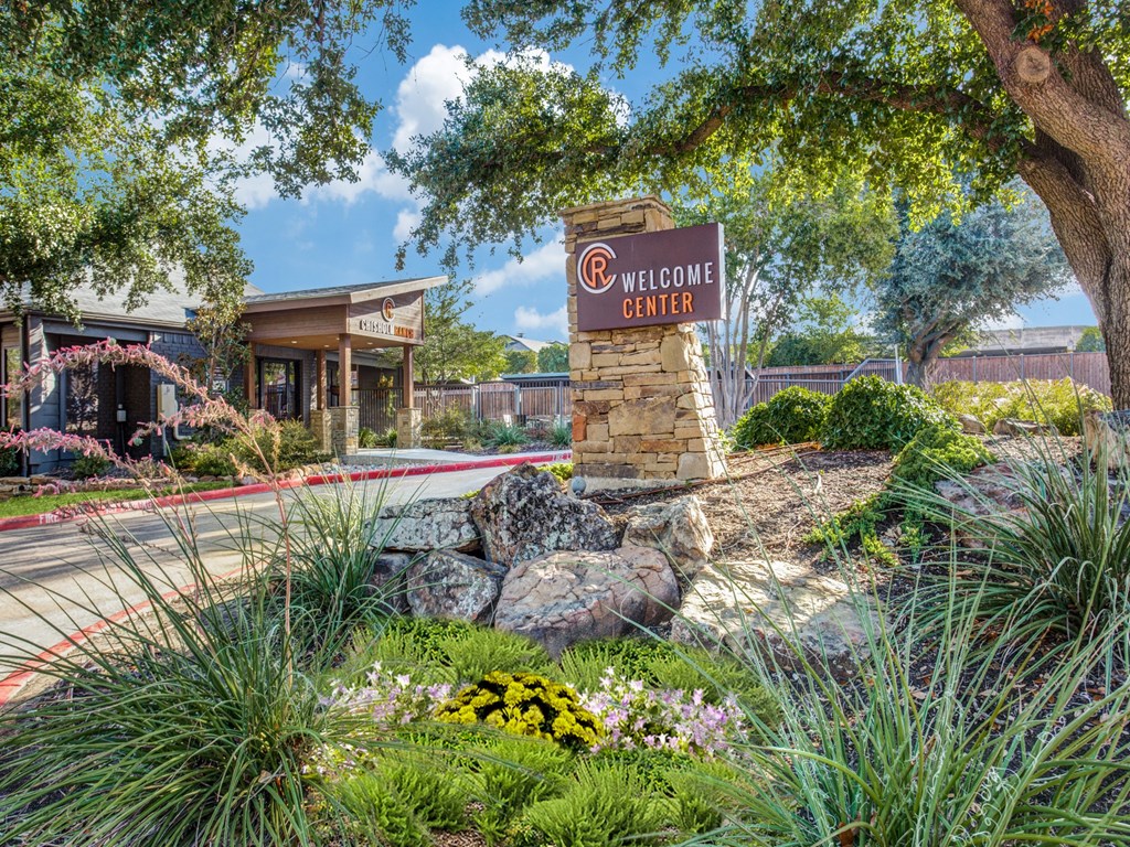 a welcome sign in front of a garden with flowers and rocks