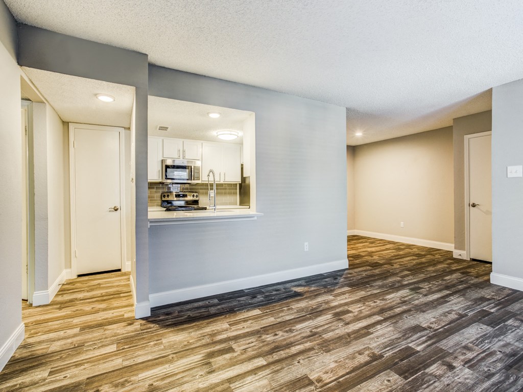 an empty living room with a kitchen in the background