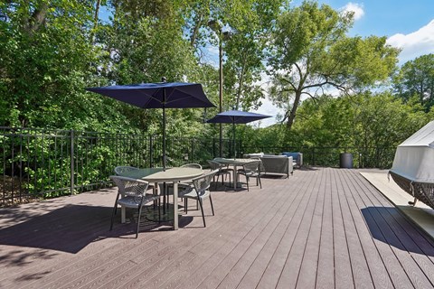 A wooden deck with chairs and tables is surrounded by green trees.