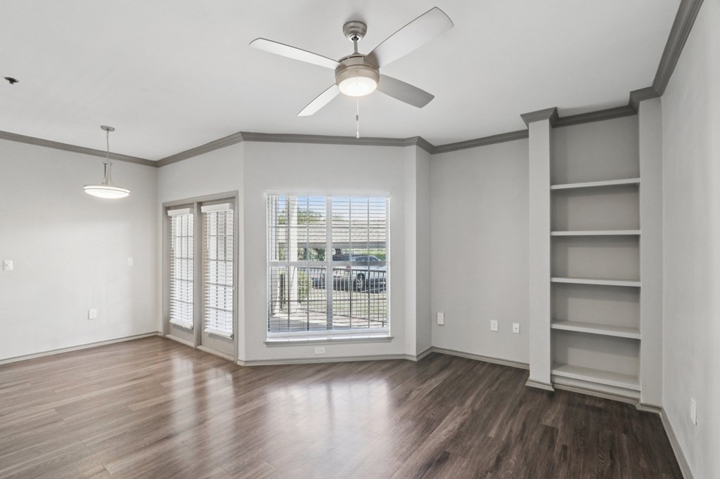 A room with a ceiling fan and a window with a view of a street.