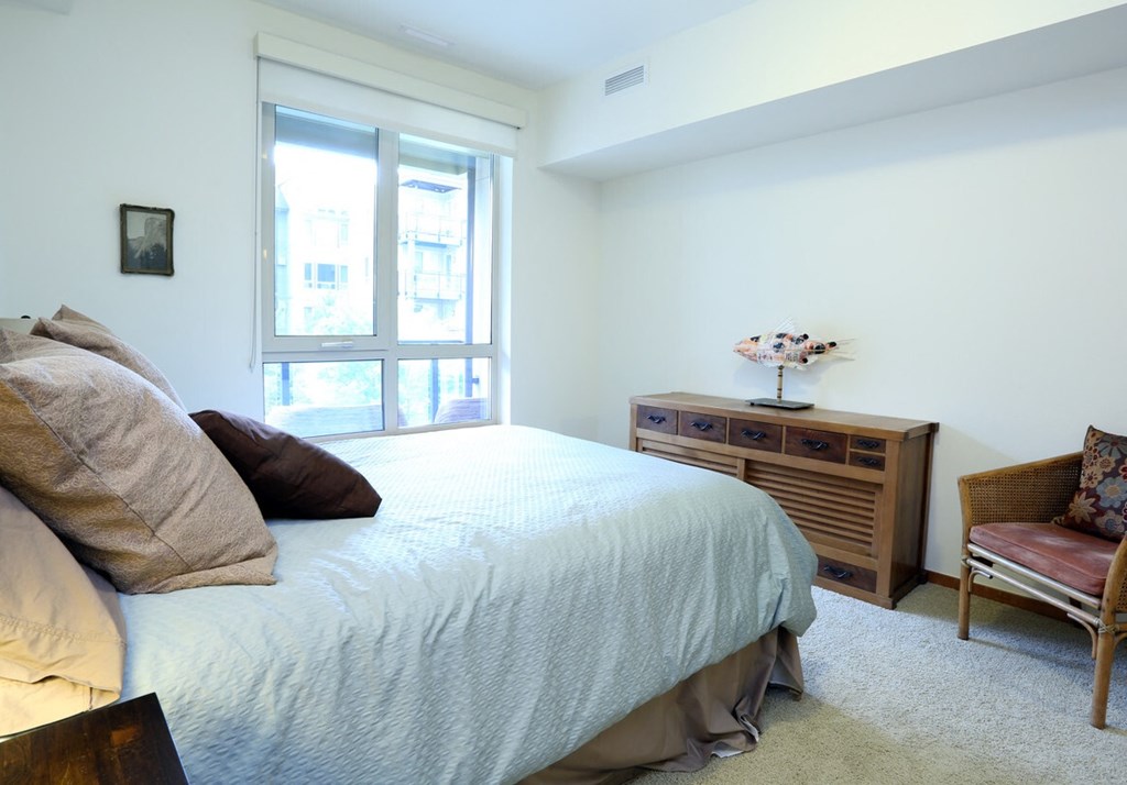 A bedroom with a bed, chair, and window.
