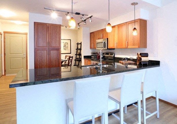 A kitchen with white chairs and a black counter top.